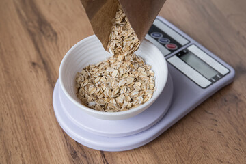 Measuring oatmeal using a kitchen scale, pouring oatmeal into a bowl on a kitchen scale