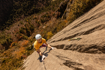 A man in a yellow shirt is climbing a rock wall