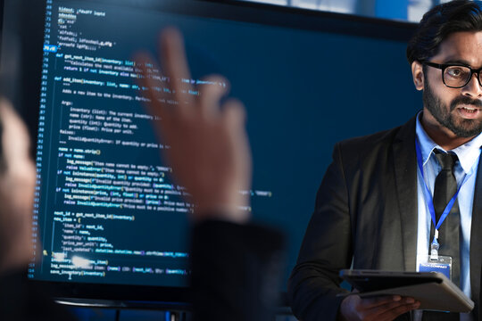 An Indian male software engineer or team lead discusses Python code for an AI algorithm. A developer in the audience raises their hand to ask a technical question during a code review.