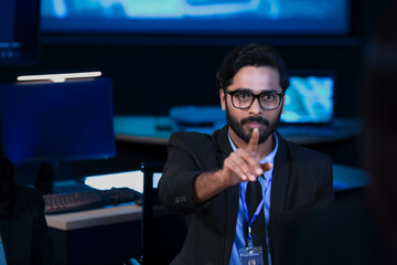 An Indian man with glasses uses a tablet to explain a project to his smiling Caucasian male colleague. They are collaborating in a modern high tech office.