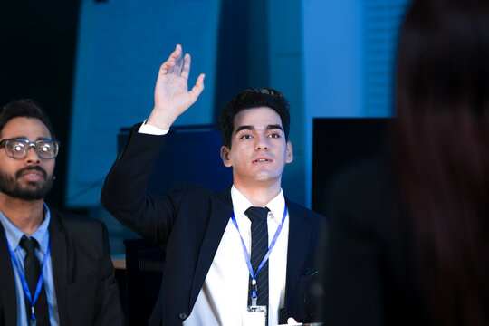 An Indian businessman holds a tablet while his Caucasian colleague uses it. The diverse team is collaborating on a project in a modern tech office at night.
