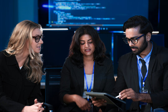 An Indian developer asks a question about AI code during a large IT department meeting. The engineering team is in a SOC, analyzing cybersecurity data on screens. - Powered by Adobe