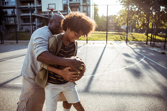 Father and teen son laughing while playing basketball on outdoor court