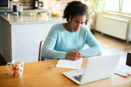 Young adult woman focused on online learning at kitchen table