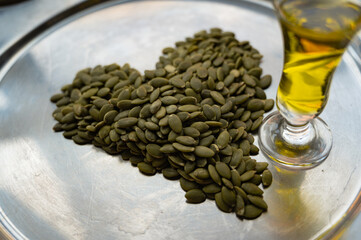 Heart-shaped pumpkin seeds with a glass of pumpkin oil – healthy food concept