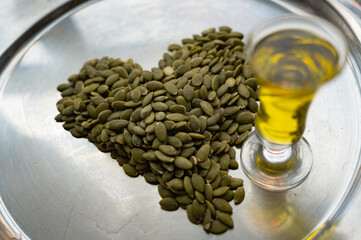 Heart-shaped pumpkin seeds with a glass of pumpkin oil – healthy food concept