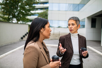 Mature businesswoman mentoring adult colleague outside modern office, serious conversation