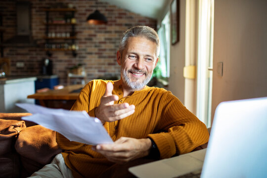 Mature man smiling on video call with paperwork at home