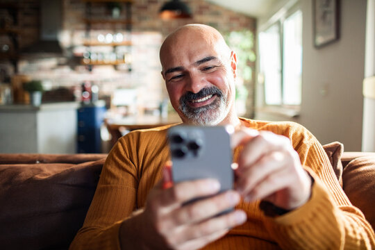 Mature man smiling while using smartphone at home