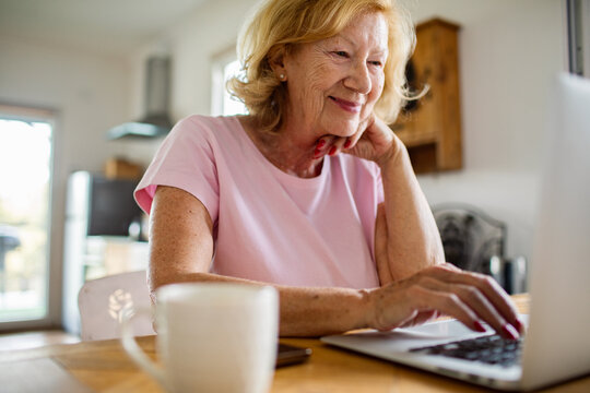 Senior woman smiling while using laptop at home kitchen
