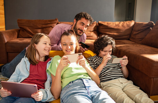 Adult parents and children smiling while gaming on phones in living room