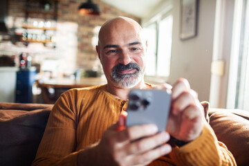 Mature man smiling while using smartphone at home