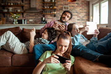 Adult parents and teens focused on screens in living room