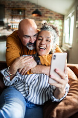 Mature couple laughing during selfie on sofa at home