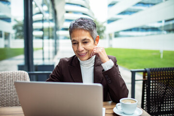 Senior woman working on laptop at outdoor cafe, content