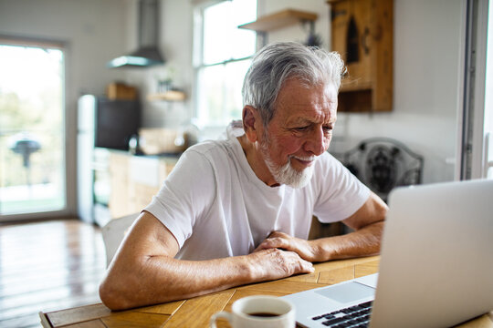 Senior man smiling while using laptop in home kitchen