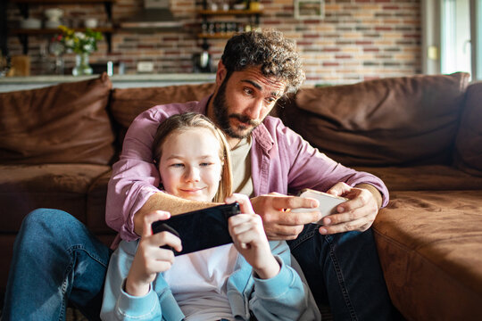 Adult father and child daughter gaming on smartphones at home, happy