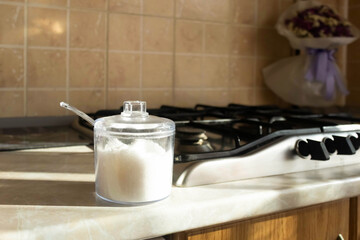 Clear sugar container placed on a countertop next to a gas stove in a bright kitchen during the day