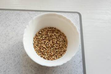 Bowl filled with small, light brown seeds placed on a white surface ready for cooking or planting purposes