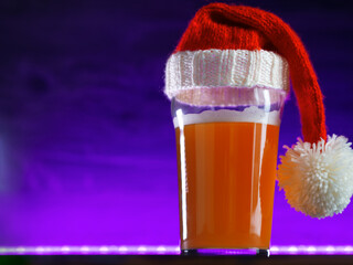 Beer glass in a Christmas hat on a purple background, copy space