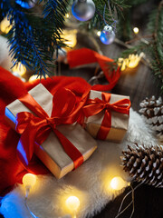 Gift boxes in craft paper with red ribbons under a Christmas tree branch on a wooden table. Cozy homely atmosphere