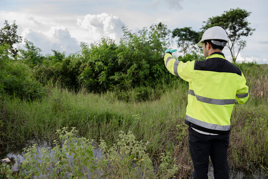 Environmental engineer wearing safety gear collecting water sample from polluted pond for contamination analysis, environmental testing, and ecological impact assessment in natural outdoor setting.