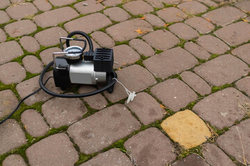 Compact air pump resting on a cobblestone path surrounded by moss and fallen leaves on a cloudy day