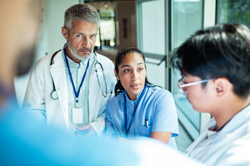 Mature doctor and adult clinicians having serious discussion in hospital corridor