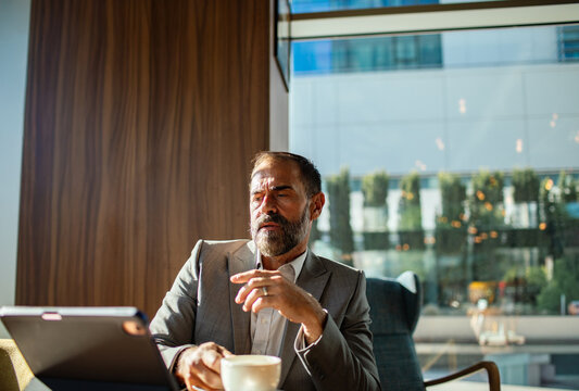 Mature businessman pensive using tablet in modern cafe