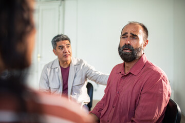 Adult men comforting upset peer in group therapy indoors