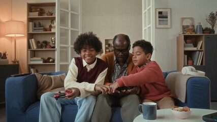 Elderly Black man and grandchildren competing in video game then team of grandfather and little grandson winning and high fiving while spending quality time on weekend in living room - Powered by Adobe
