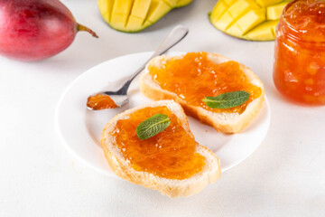 Golden mango marmalade jam with fresh ripe whole and diced mango fruits n white kitchen table background, homemade sweet preserves 