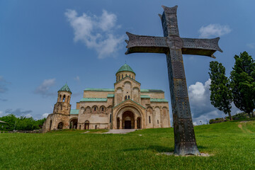 Cathedral with green domes behind large metal cross on hill