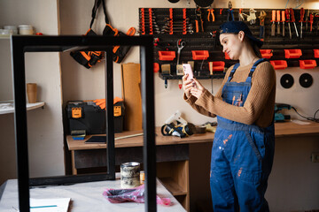 Female mechanic repair worker photographing metal structure while working in small furniture workshop