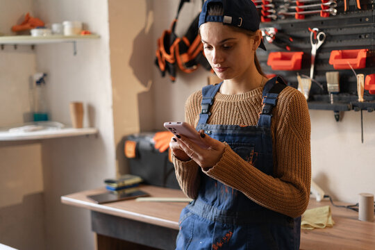 female worker messaging on mobile phone while standing near workbench in mechanic workshop - Powered by Adobe