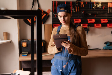 Small business owner in blue overalls ordering construction supplies online using digital tablet