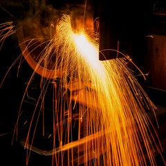 Metal grinding generates bright orange sparks in dark factory