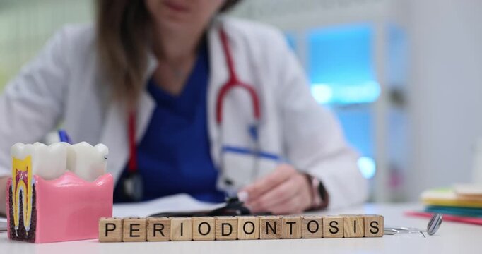 Woman dentist writes down stages of treatment plan for patient at appointment. Wooden cubes neatly arranged on surface of desk form word Periodontosis