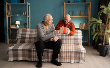 Adult son visiting elderly father to celebrate Father's Day and presenting a wrapped gift