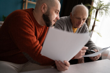 Adult son helping retired father pay bills and sort out mortgage documents while sitting at home