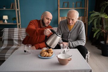 Elderly retired father and adult son spending quality family time drinking tea together on couch