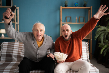Happy elderly father and middle-aged son football fans celebrating favorite team's victory at home