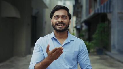 Portrait of positive Indian man says Thank You with sign language on old city street. Deaf Hindu bearded male in blue shirt expresses gratefulness by gestures in urban district