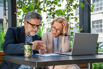 Business partners stressed over failed project using laptop in green office with plants