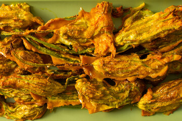 Crispy, golden-brown deep-fried zucchini flowers sit on a light green plate. They are perfect for sharing at a summer gathering, offering a delicious flavor and unique texture