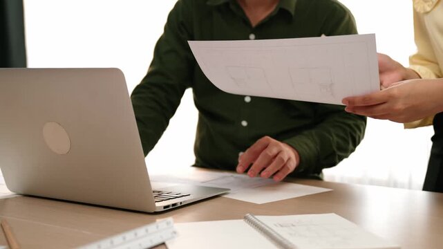 Architect and engineer compare hand writing draft with construction blueprint detail display in laptop for accurate design, measurement tool and plan on table at modern office. Closeup. Delineation.