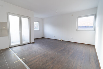 Empty apartment room with white walls and a dirty wood laminate floor. Empty apartment room. Room apartment under renovation