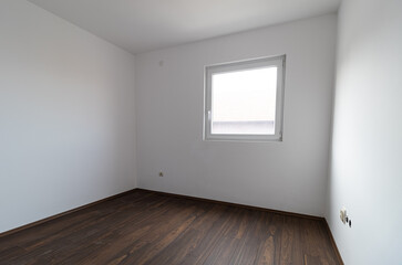 Fototapeta premium Small empty apartment room with white walls and a dirty wood laminate floor. Empty apartment room. Room apartment under renovation