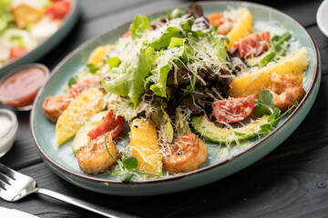 Gourmet salad with grilled shrimp, fresh orange slices, avocado, lettuce leaves, and grated Parmesan cheese