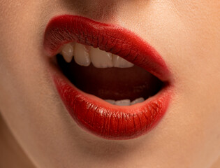 Fototapeta premium Dramatic close-up of the lower face, highlighting a woman's mouth with full lips painted in a rich, matte, deep red color, showcasing beauty, fashion, and cosmetic product quality.